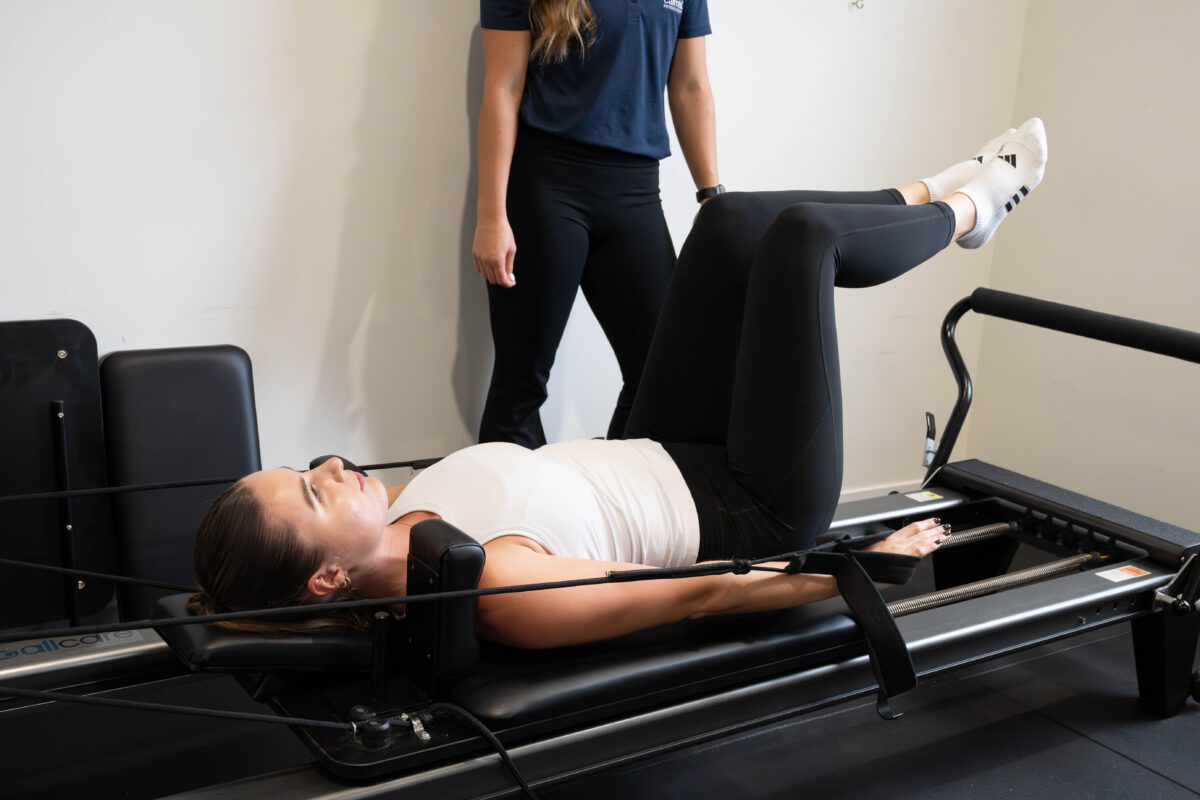 A physiotherapist guiding a patient through Pilates on a reformer
