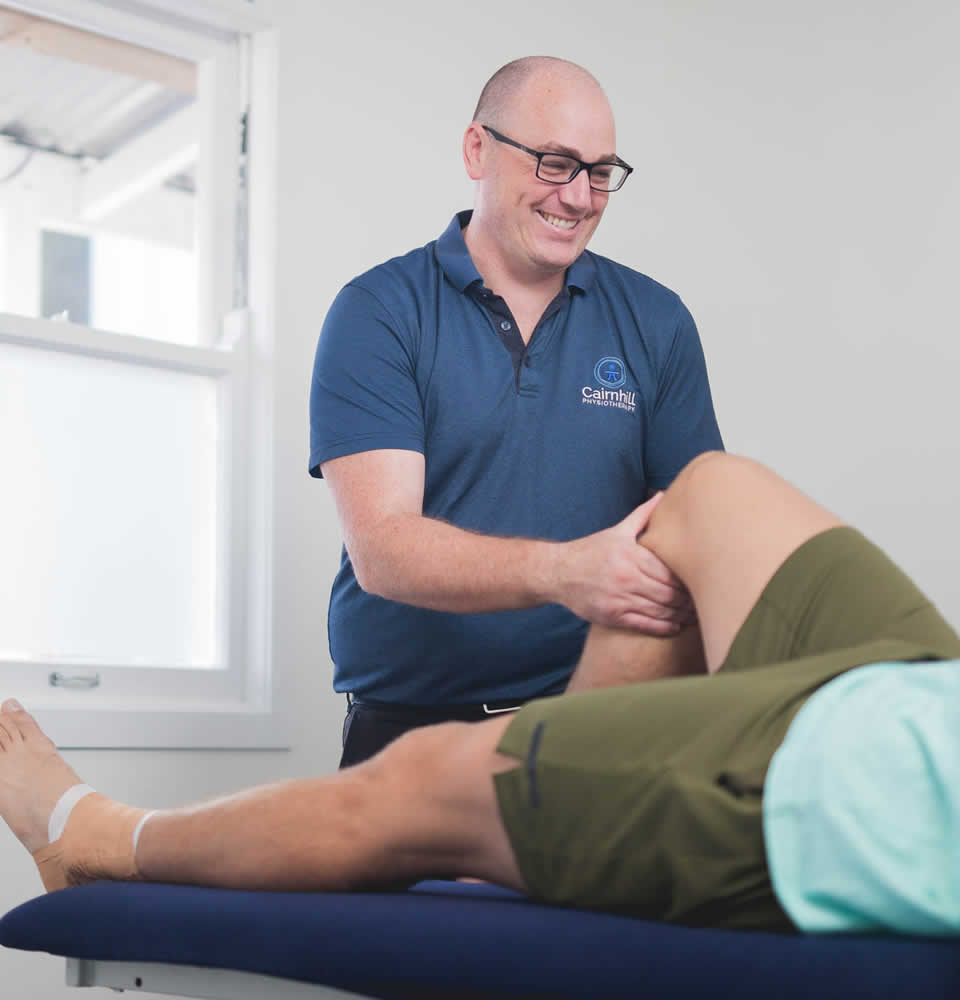 A physiotherapist assessing a patient’s knee on the treatment bed