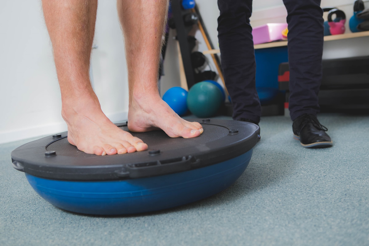 A patient balancing barefoot on a balance trainer in the rehabilitation gym